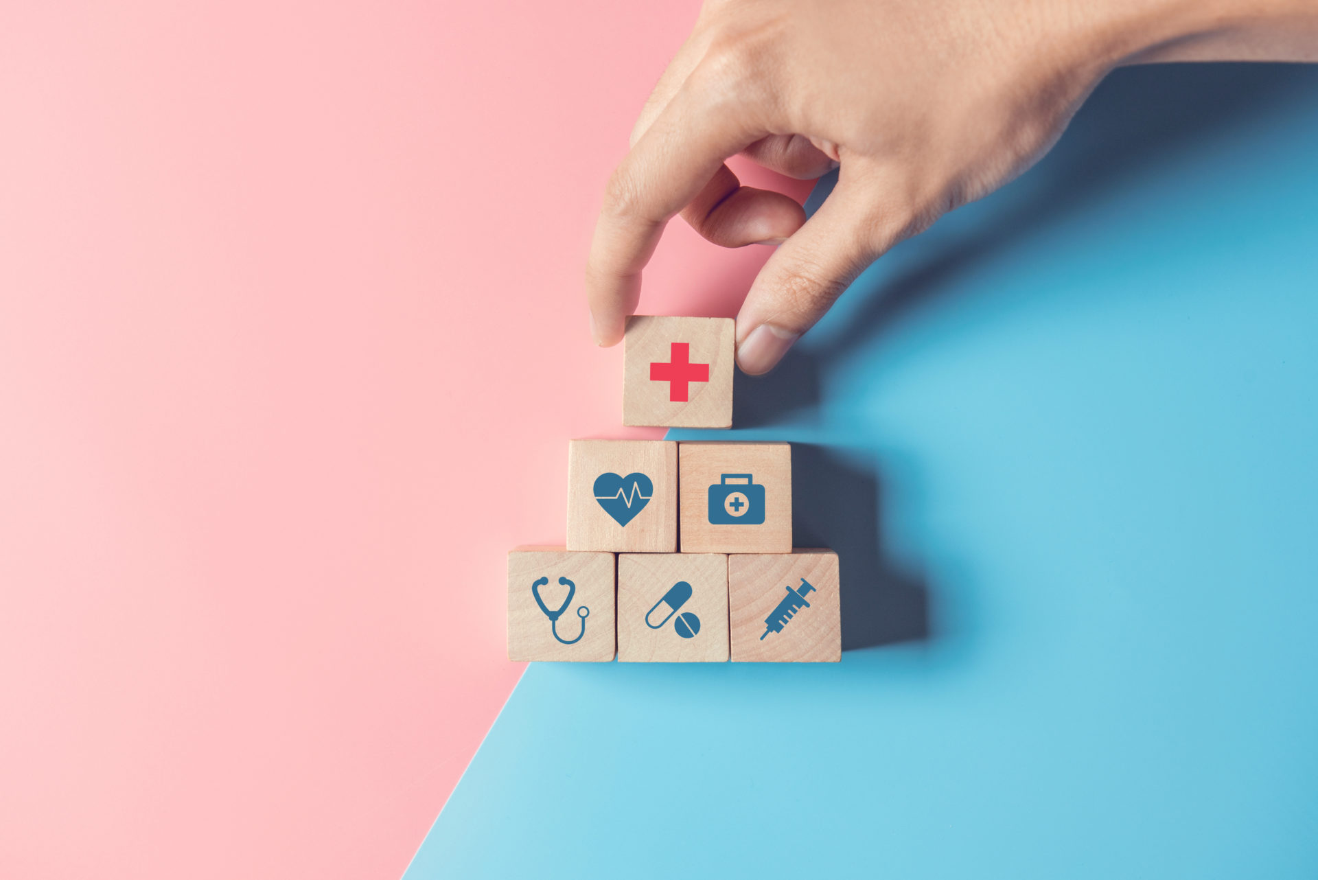 Health Insurance Concept, Hand of man arranging wood cube stacking with icon healthcare medical on pastel blue and pink background, copy space.